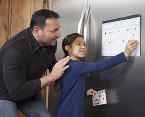 Man watching girl put sticker on calendar page.