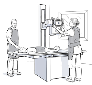 Boy lying on back on table under X-ray machine. Health care provider is moving machine into place over boy’s feet.